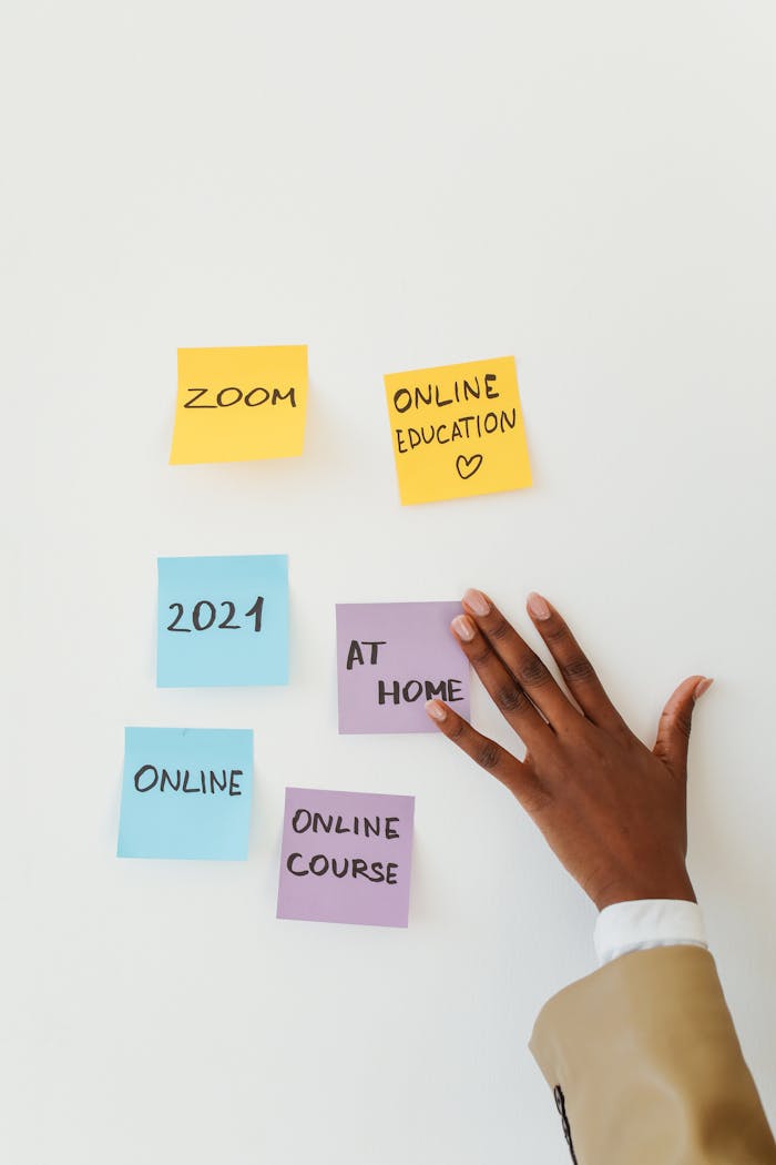 Sticky notes about online education and a hand on a white wall, symbolizing remote learning.